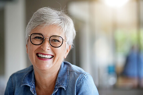 Senior woman with glasses and denim jacket smiling