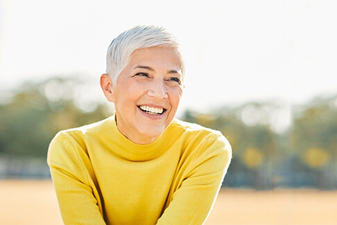 Senior woman in yellow shirt sitting in field and smiling