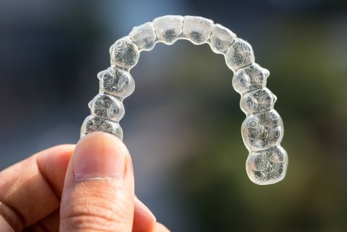Hand holding a clear aligner outdoors