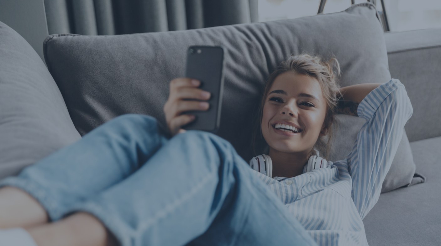 Laughing woman lying on couch while looking at cell phone