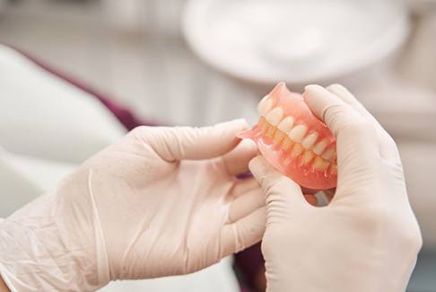 Gloved hands holding full upper and lower dentures