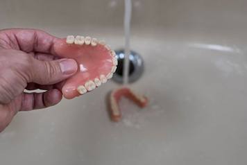 Person rinsing their dentures in bathroom sink