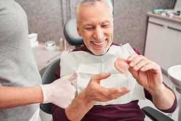 a patient smiling and holding his new dentures