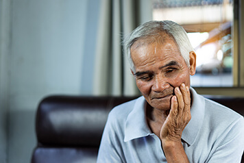 An older man feeling an ache from his dental implant