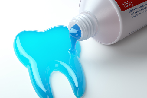 Blue toothpaste being squeezed out into the shape of a tooth